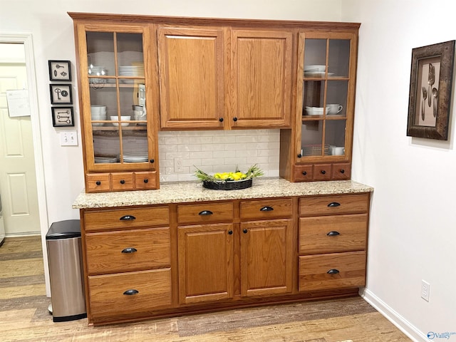2072 Madison Villas Way Unit 2072, Madison, AL 35758 - kitchen featuring brown cabinetry, light wood finished floors, tasteful backsplash, light stone counters, and glass insert cabinets