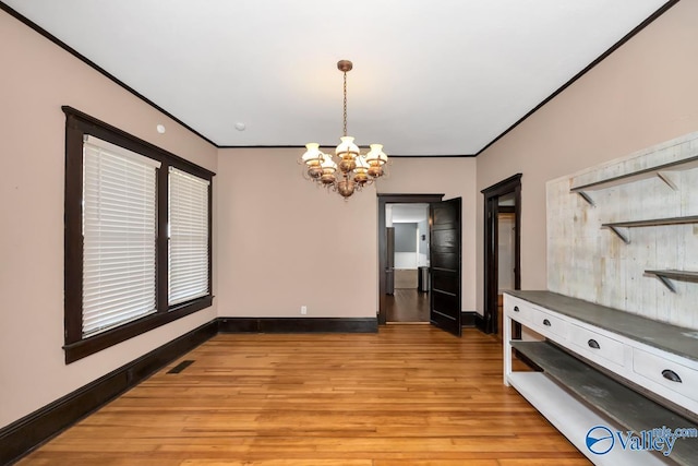 unfurnished dining area with ornamental molding, light wood-type flooring, and a notable chandelier