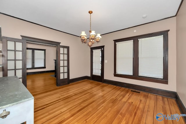 unfurnished dining area featuring wood-type flooring, ornamental molding, and an inviting chandelier