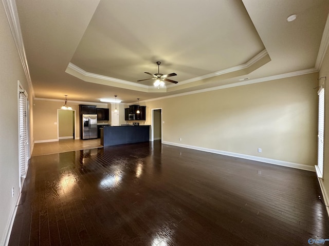 unfurnished living room with a tray ceiling, dark hardwood / wood-style floors, ornamental molding, and ceiling fan