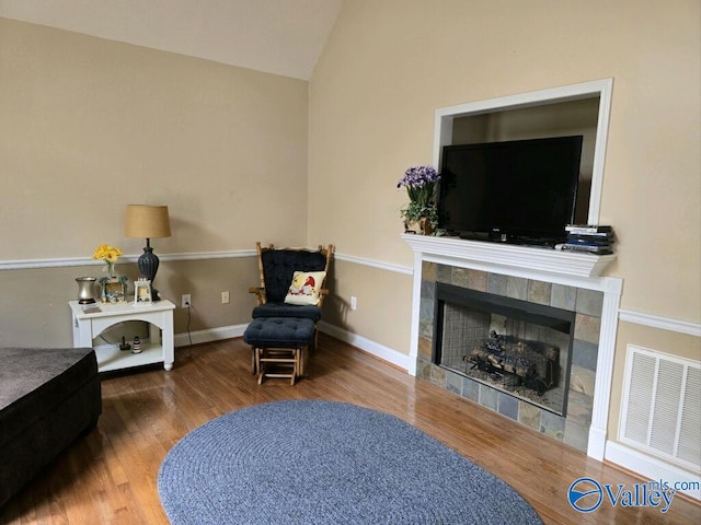 sitting room with lofted ceiling, wood-type flooring, and a tiled fireplace