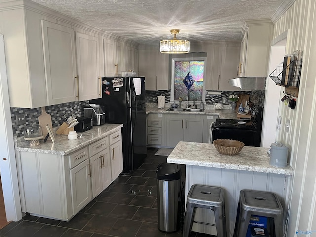 kitchen with light stone counters, white cabinets, black appliances, sink, and a kitchen bar