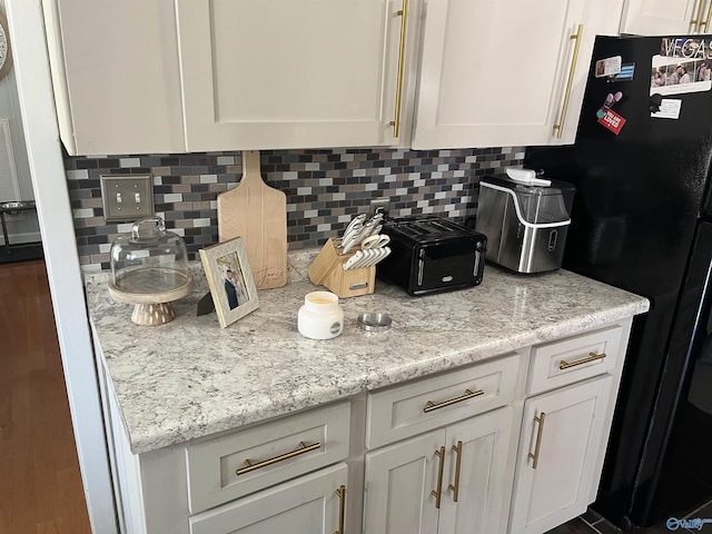 kitchen with light stone counters, white cabinets, decorative backsplash, and black fridge