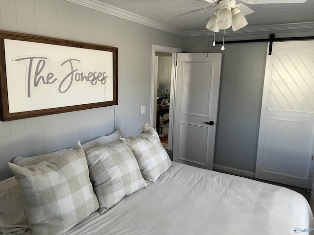 bedroom featuring a textured ceiling, ornamental molding, ceiling fan, and a barn door