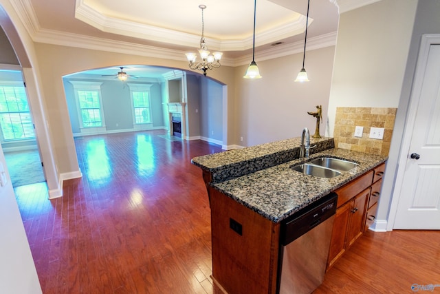 kitchen featuring a raised ceiling, hanging light fixtures, dark stone counters, stainless steel dishwasher, and sink