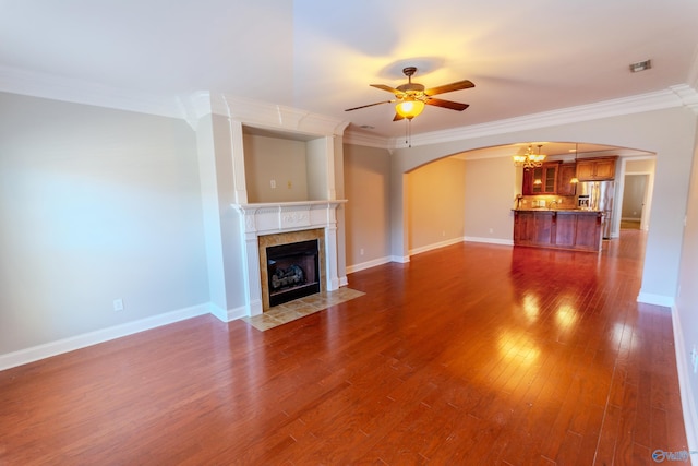 unfurnished living room with ceiling fan, a tiled fireplace, dark wood-type flooring, and ornamental molding