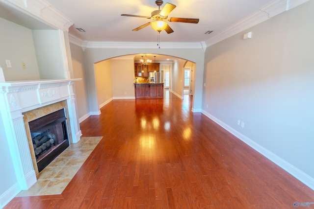 unfurnished living room featuring ceiling fan with notable chandelier, a fireplace, dark hardwood / wood-style flooring, and crown molding