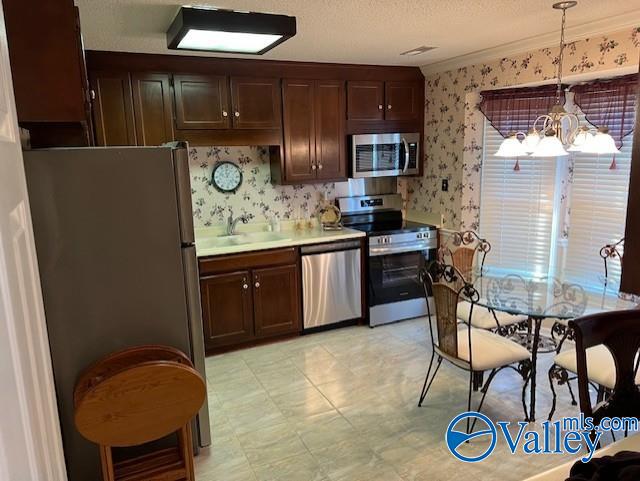 kitchen with an inviting chandelier, crown molding, a textured ceiling, decorative light fixtures, and appliances with stainless steel finishes