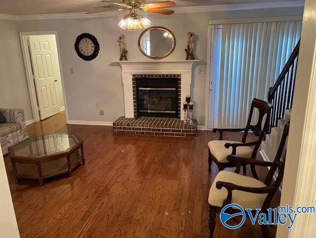 sitting room with a brick fireplace, ceiling fan, dark wood-type flooring, and ornamental molding