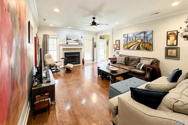 living room featuring a tile fireplace, light hardwood / wood-style floors, ceiling fan, and ornamental molding