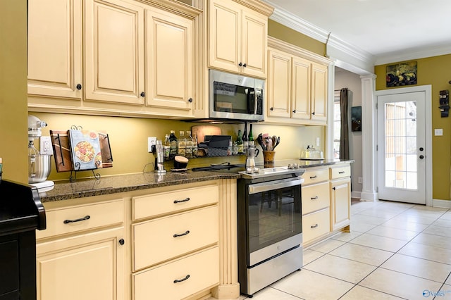 kitchen with dark stone countertops, appliances with stainless steel finishes, light tile patterned flooring, crown molding, and cream cabinets