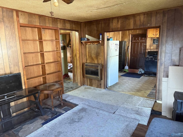 kitchen with black gas stove, white fridge, heating unit, and wood walls