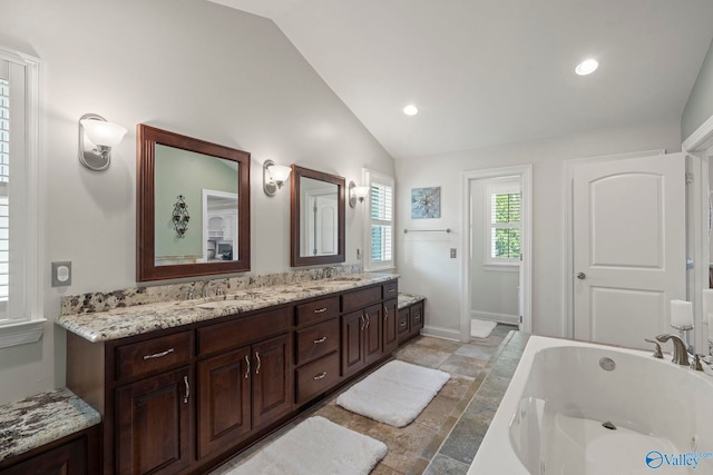 406 Zandale Dr SW, Huntsville, AL 35801 - bathroom with vaulted ceiling, a garden tub, stone tile flooring, double vanity, and baseboards