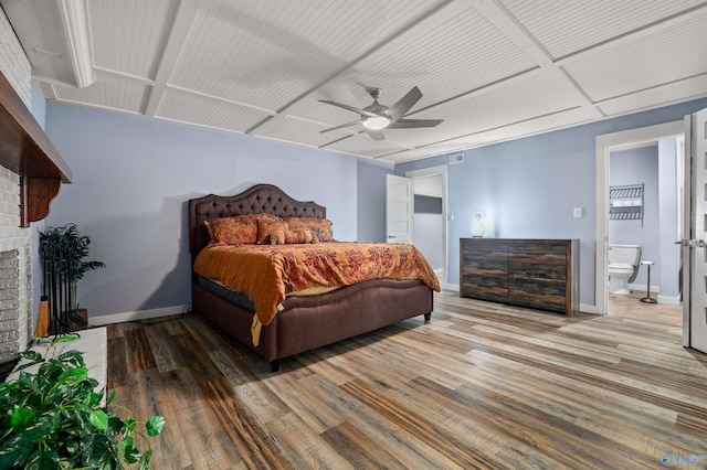 bedroom with wood-type flooring, a fireplace, ensuite bath, and ceiling fan