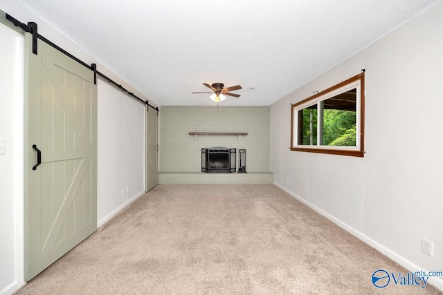 unfurnished living room with a barn door, ceiling fan, light carpet, a fireplace, and baseboards