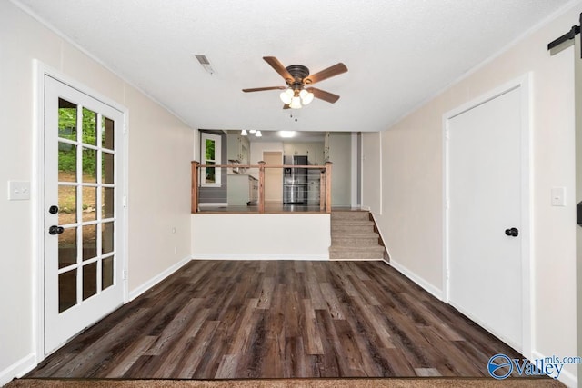 unfurnished living room with a barn door, visible vents, dark wood-type flooring, baseboards, and ceiling fan