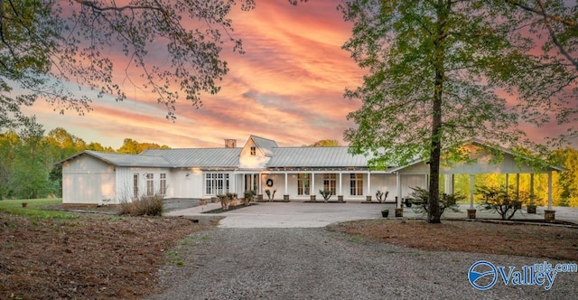 ranch-style house featuring metal roof, covered porch, a chimney, and gravel driveway