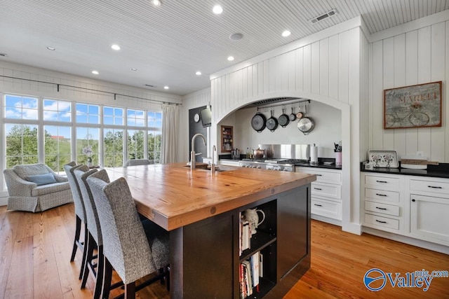 kitchen with butcher block counters, visible vents, a sink, light wood-style floors, and a center island with sink