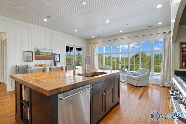 kitchen with a sink, wood counters, open floor plan, light wood-style floors, and appliances with stainless steel finishes