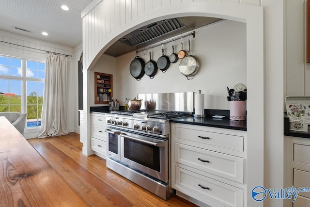 kitchen featuring dark countertops, range with two ovens, visible vents, arched walkways, and light wood-style floors