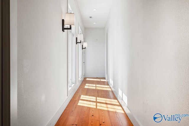 hall featuring baseboards, recessed lighting, and light wood-type flooring