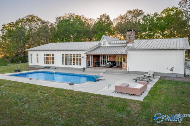 rear view of house featuring a patio, a chimney, metal roof, a yard, and an outdoor pool