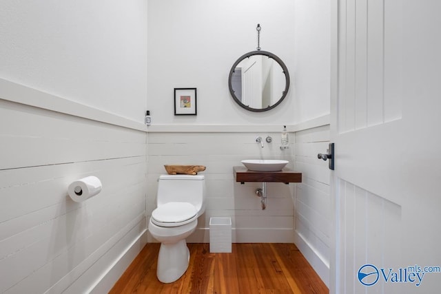 bathroom with a sink, wainscoting, toilet, and wood finished floors