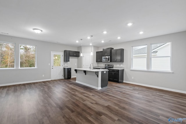 kitchen with decorative light fixtures, stainless steel appliances, an island with sink, sink, and dark hardwood / wood-style floors