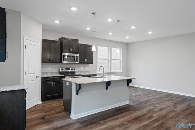 kitchen featuring decorative light fixtures, stainless steel appliances, an island with sink, sink, and dark wood-type flooring