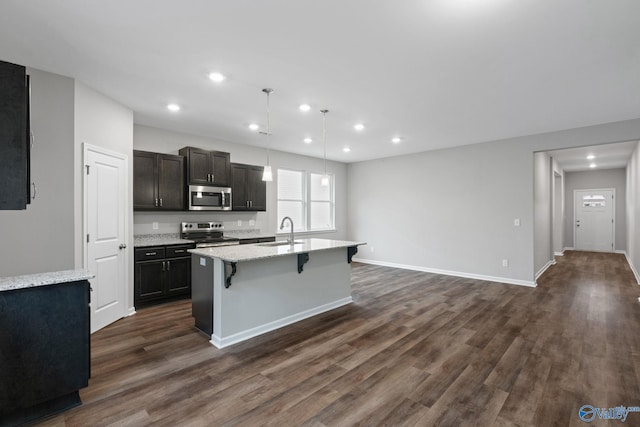 kitchen with stainless steel appliances, pendant lighting, sink, dark hardwood / wood-style floors, and a kitchen island with sink