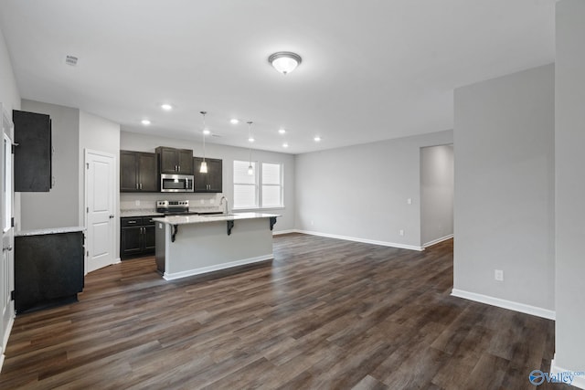 kitchen featuring appliances with stainless steel finishes, pendant lighting, dark hardwood / wood-style flooring, and a center island with sink