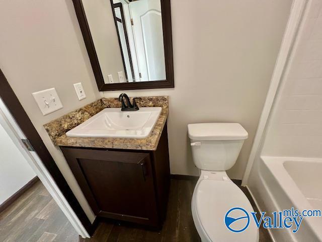 bathroom with hardwood / wood-style floors, vanity, toilet, and a tub