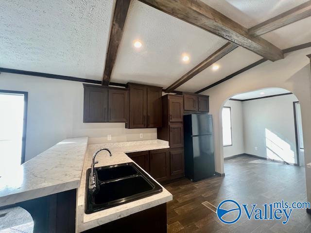 kitchen featuring black fridge, a textured ceiling, sink, vaulted ceiling with beams, and dark hardwood / wood-style floors