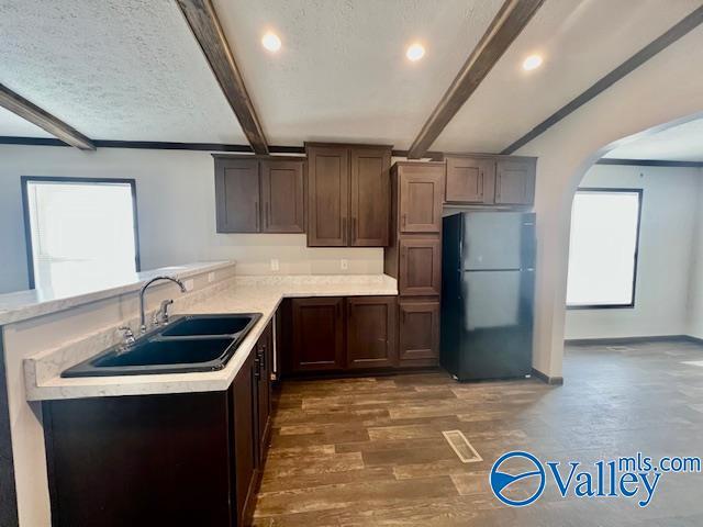 kitchen featuring dark hardwood / wood-style flooring, black fridge, a textured ceiling, sink, and beamed ceiling