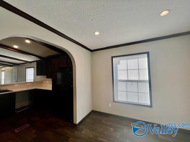 kitchen with dark wood-type flooring, black refrigerator, sink, ornamental molding, and a textured ceiling