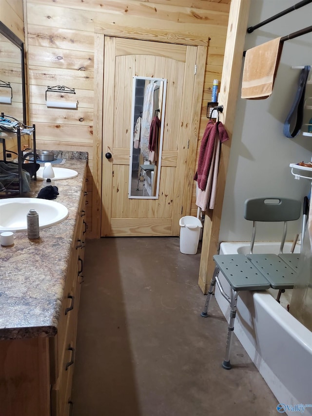 full bath with concrete floors, double vanity, wooden walls, and a sink