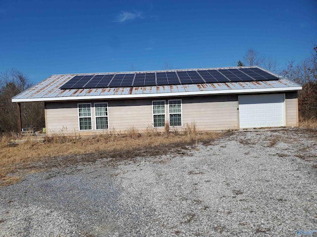 exterior space with a garage, roof mounted solar panels, metal roof, and driveway