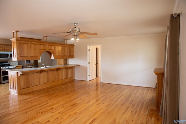 kitchen with ceiling fan, light wood-style flooring, stainless steel appliances, a kitchen bar, and crown molding