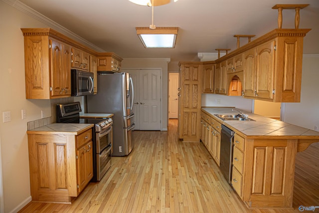 kitchen with tile countertops, light wood-style flooring, appliances with stainless steel finishes, ornamental molding, and a sink