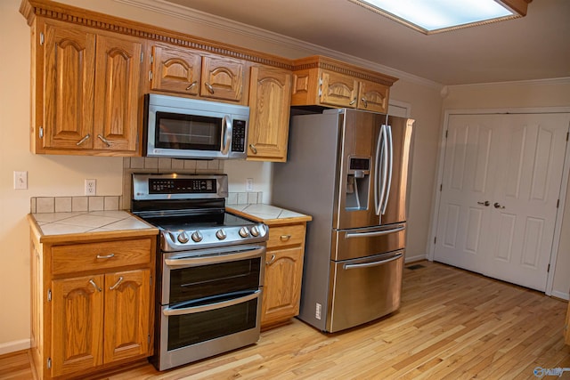 kitchen featuring light wood-style flooring, tile counters, stainless steel appliances, and crown molding