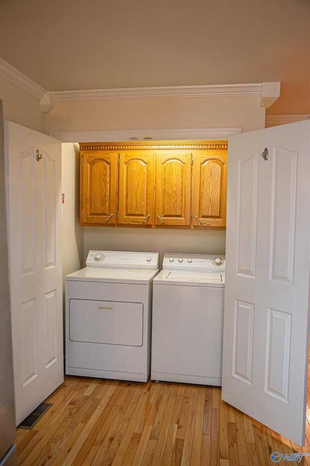 clothes washing area with ornamental molding, light wood-type flooring, cabinet space, and washing machine and clothes dryer