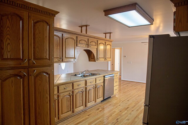 kitchen with tile countertops, stainless steel appliances, a sink, baseboards, and light wood finished floors