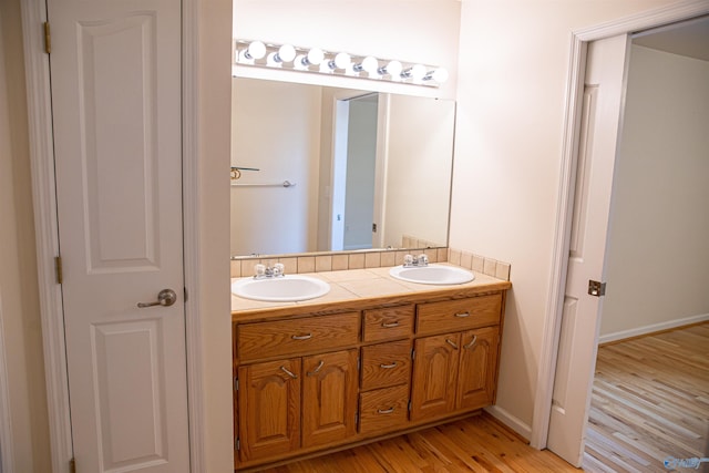 full bathroom featuring double vanity, a sink, baseboards, and wood finished floors