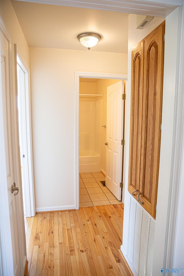 corridor with light wood finished floors, visible vents, and baseboards