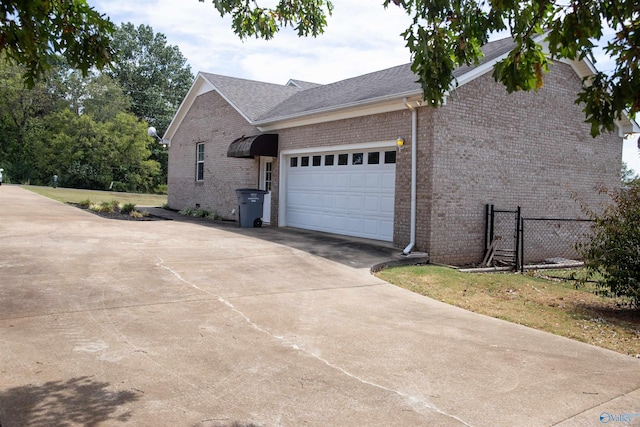 view of property exterior featuring brick siding, driveway, an attached garage, and fence