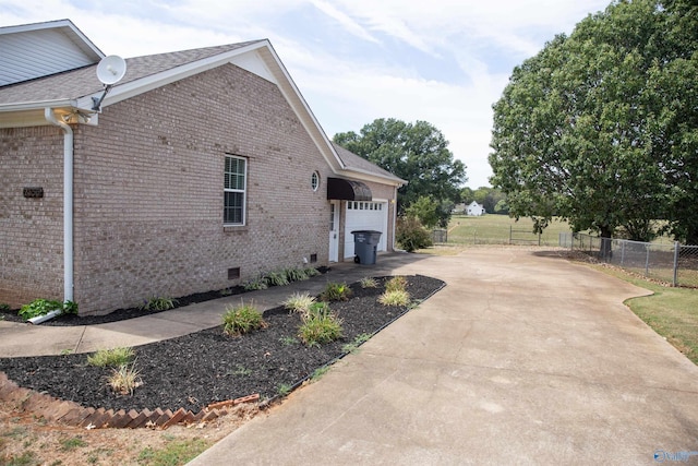 view of property exterior featuring brick siding, crawl space, fence, a garage, and driveway