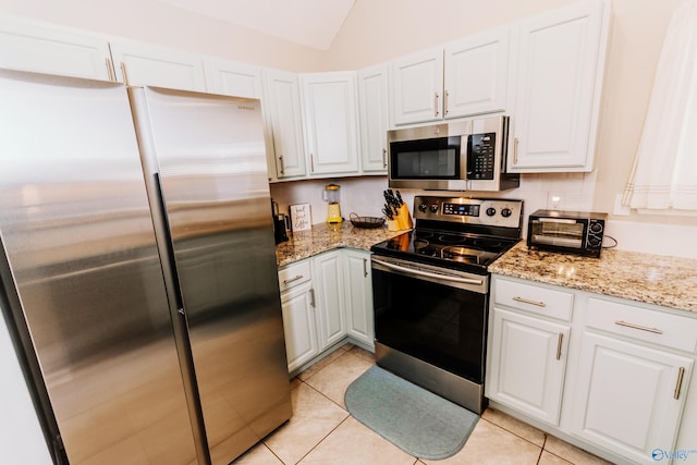 kitchen with white cabinetry, stainless steel appliances, light stone counters, and light tile patterned floors