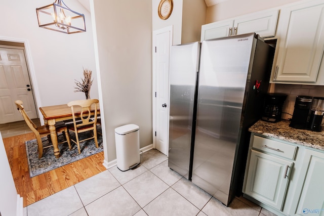 kitchen featuring stainless steel refrigerator, tasteful backsplash, dark stone counters, hanging light fixtures, and light tile patterned floors