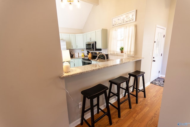 kitchen with high vaulted ceiling, a breakfast bar area, light hardwood / wood-style floors, kitchen peninsula, and stainless steel appliances