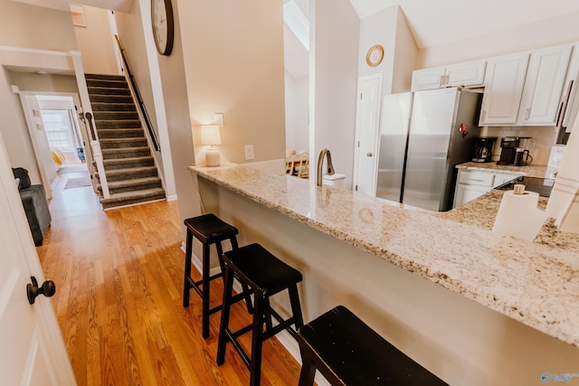 kitchen featuring stainless steel refrigerator, a kitchen bar, light stone countertops, and white cabinets